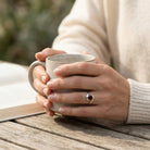 [KI] Granatring aus Silber getragen beim Lesen mit einer Tasse