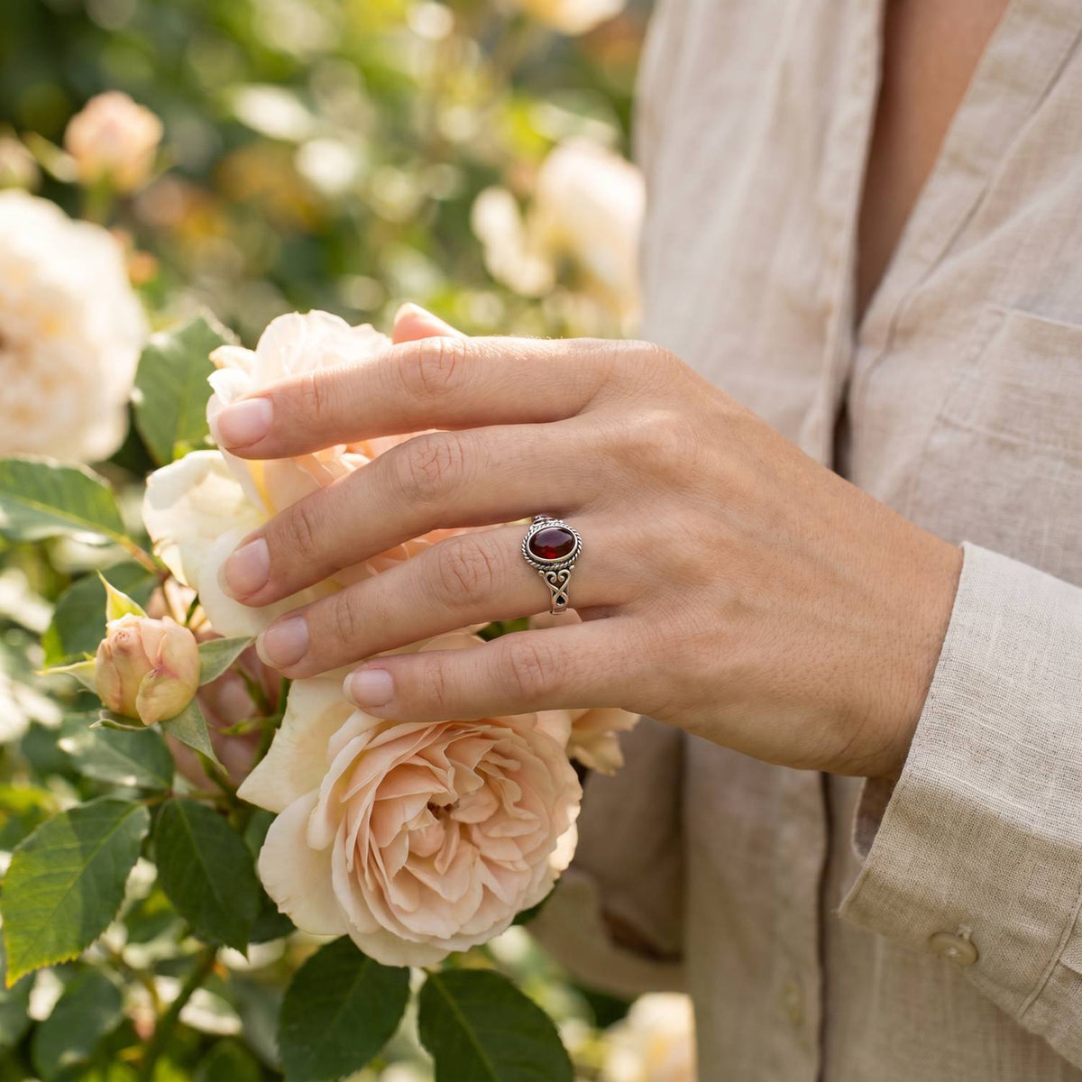 Silberring mit Granat an der Hand zwischen Blumen