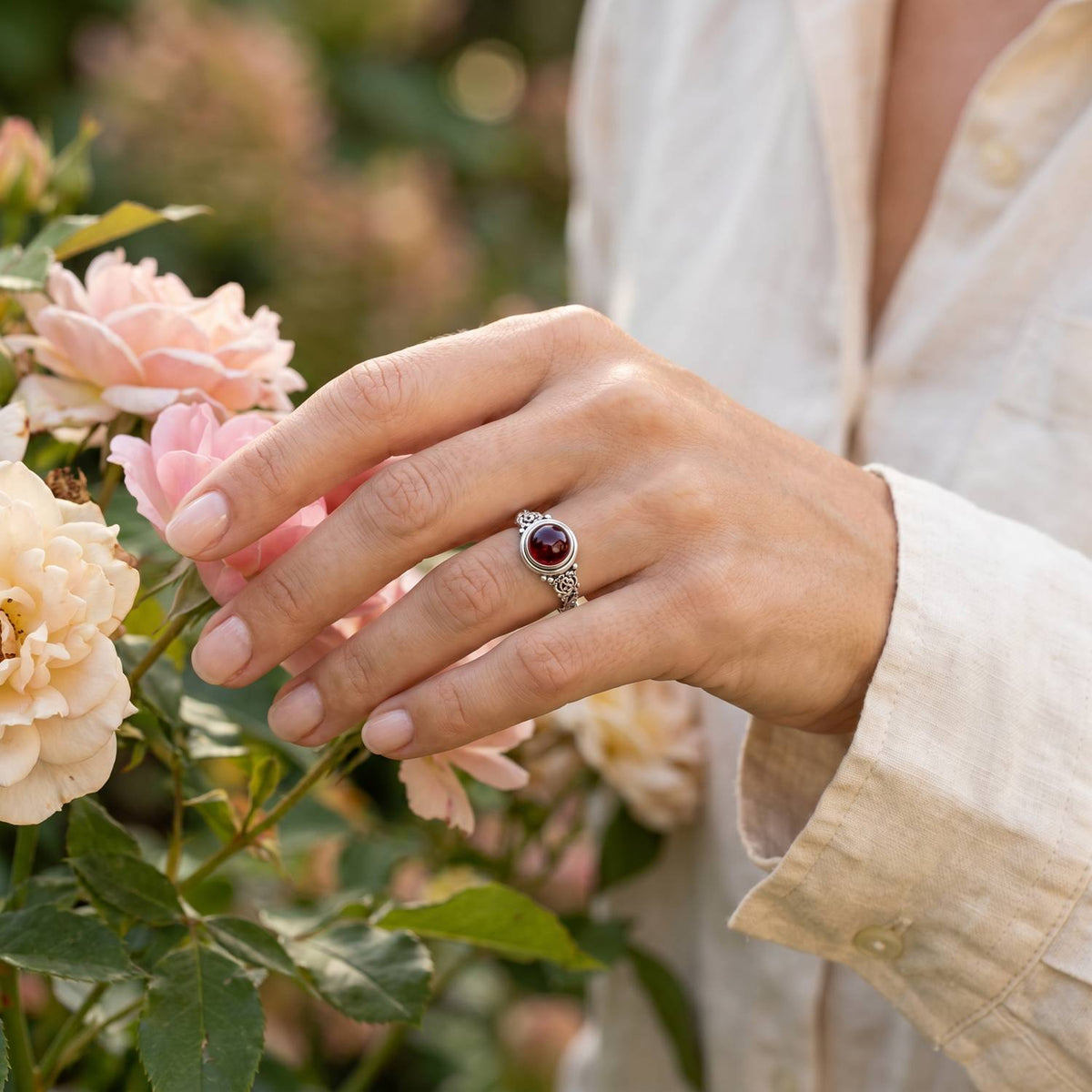 Silberring mit Granat an der Hand zwischen Blumen
