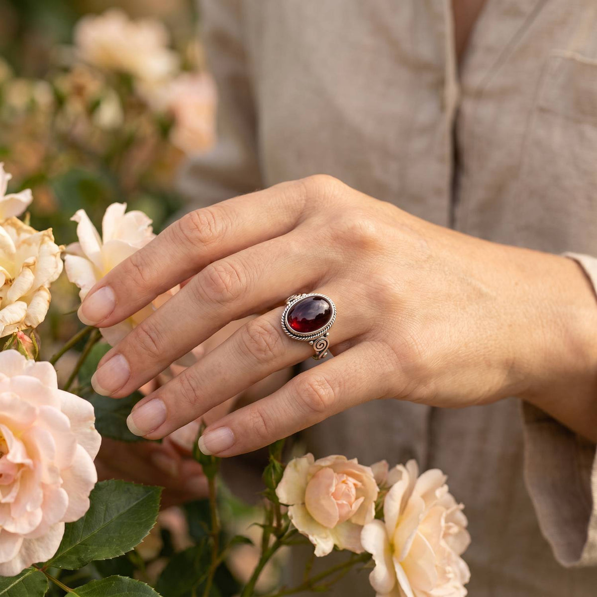 Silberring mit Granat an der Hand zwischen Blumen