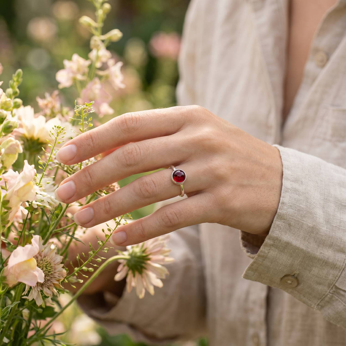 Silberring mit Granat an der Hand zwischen Blumen