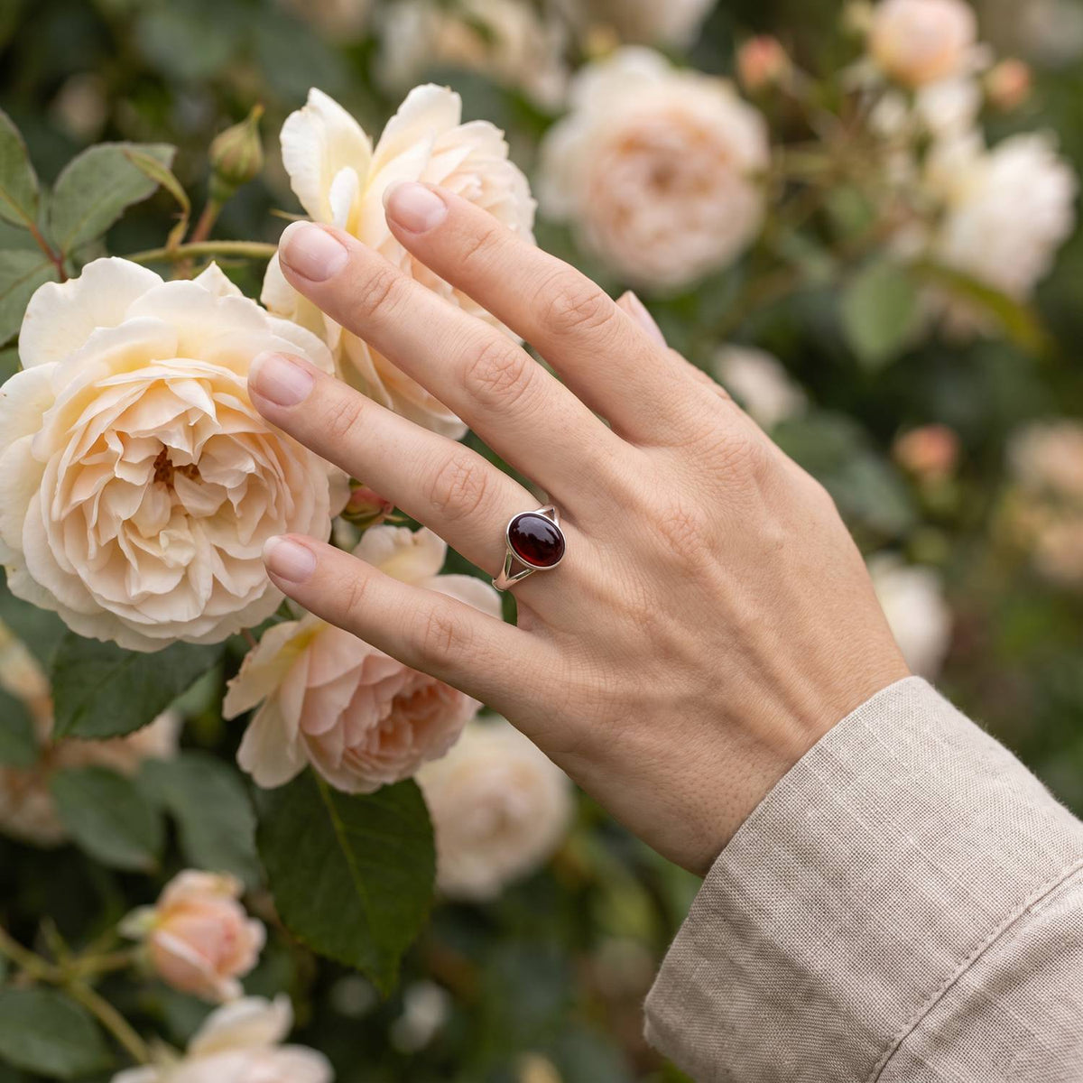 Silberring mit Granat an der Hand zwischen Blumen