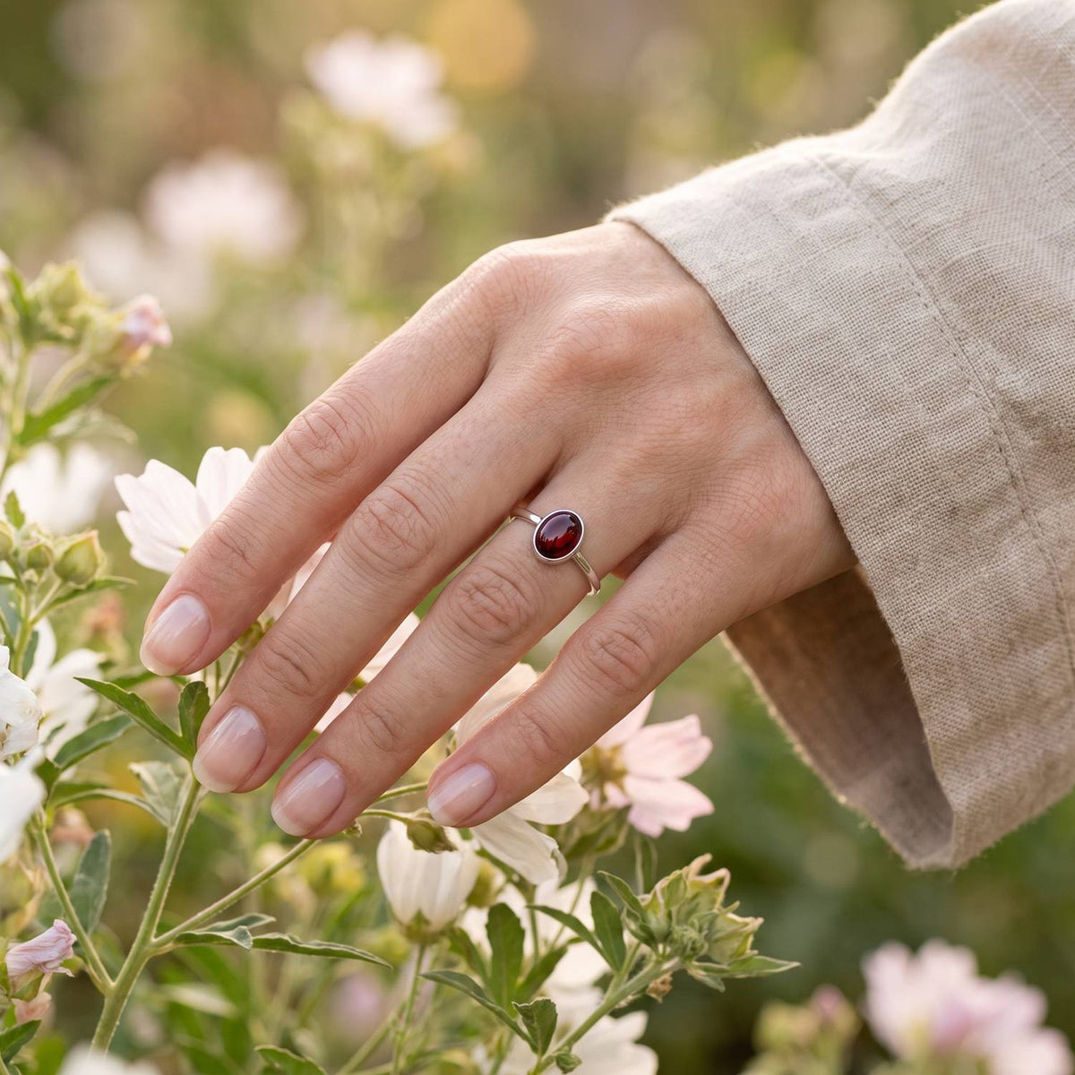 Silberring mit Granat an der Hand zwischen Blumen