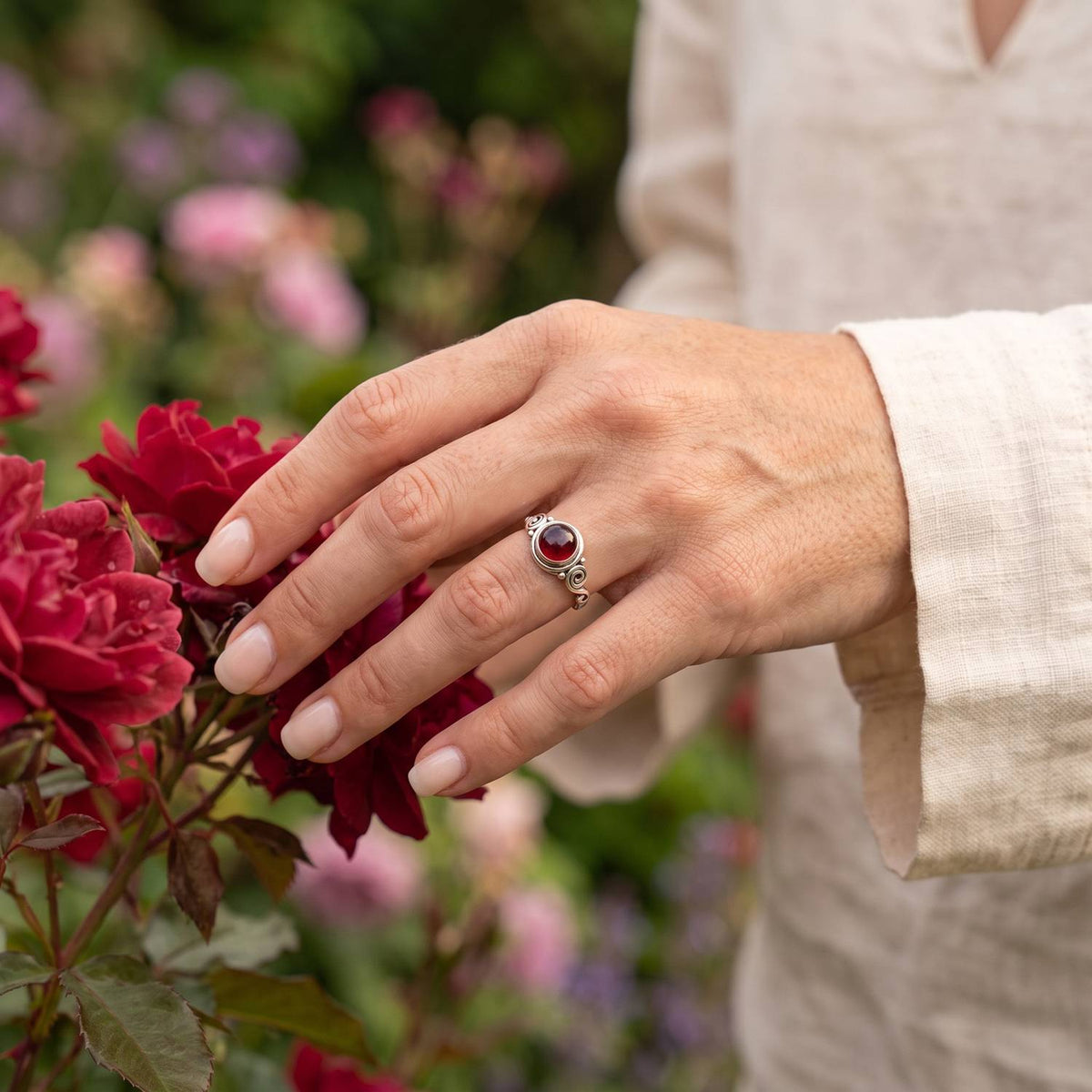 Silberring mit Granat an der Hand zwischen Blumen
