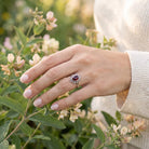 [KI] Silberring mit Granat an der Hand zwischen Blumen