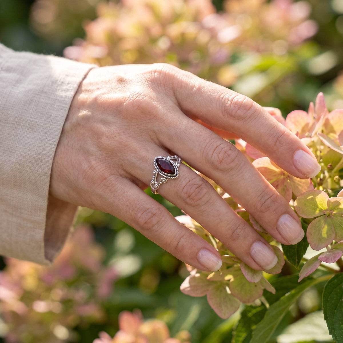 Silberring mit Granat an der Hand zwischen Blumen
