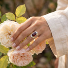 [KI] Silberring mit Granat an der Hand zwischen Blumen