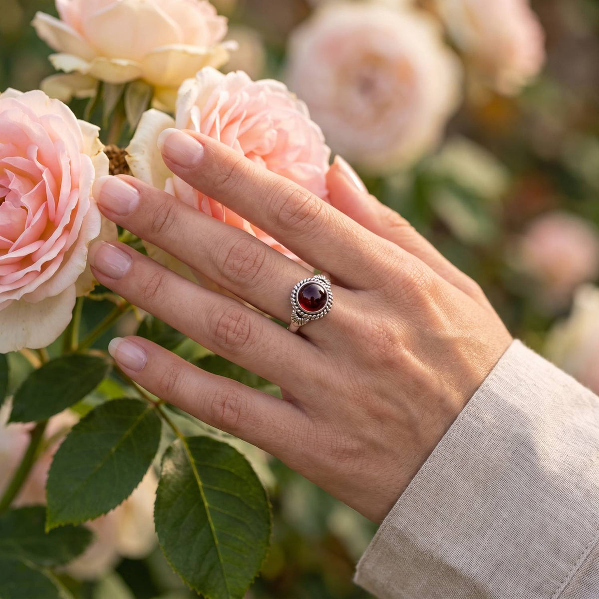 Silberring mit Granat an der Hand zwischen Blumen