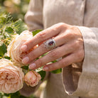 [KI] Silberring mit Granat an der Hand zwischen Blumen