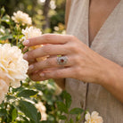 [KI] Silberring mit Granat an der Hand zwischen Blumen