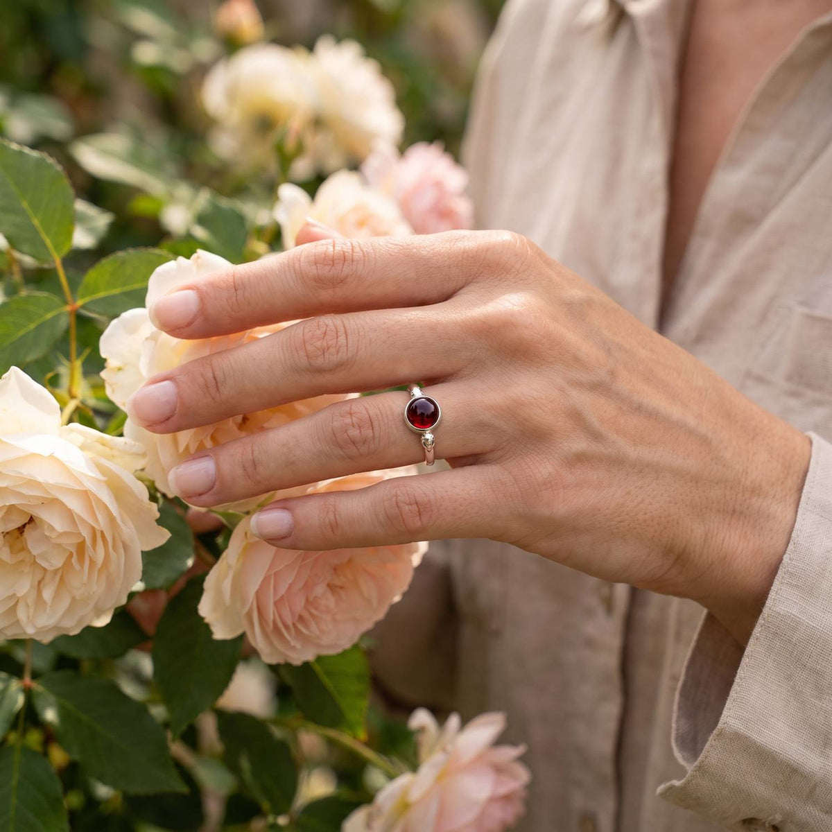 Silberring mit Granat an der Hand zwischen Blumen