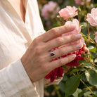 [KI] Silberring mit Granat an der Hand zwischen Blumen