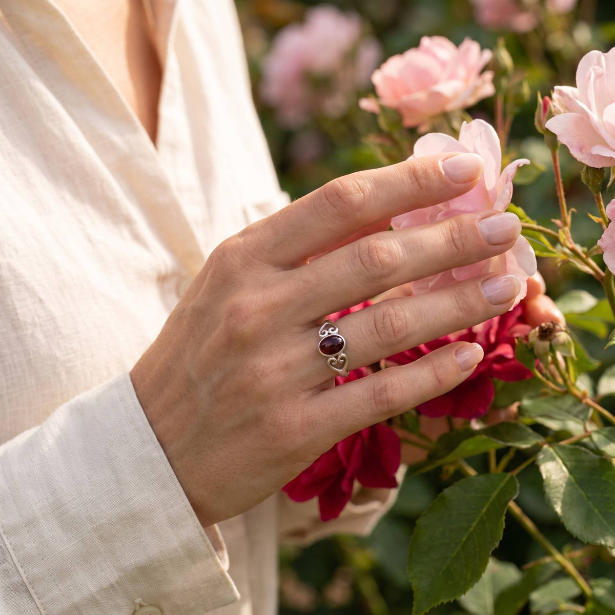 Silberring mit Granat an der Hand zwischen Blumen