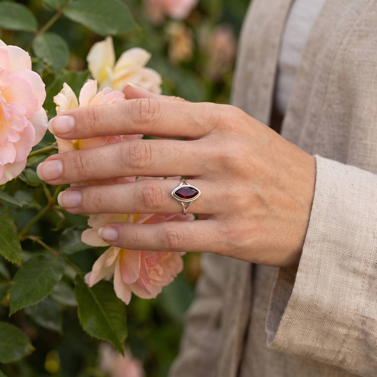 Silberring mit Granat an der Hand zwischen Blumen