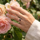 [KI] Silberring mit Granat an der Hand zwischen Blumen