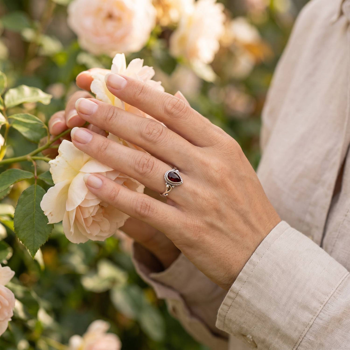 Silberring mit Granat an der Hand zwischen Blumen