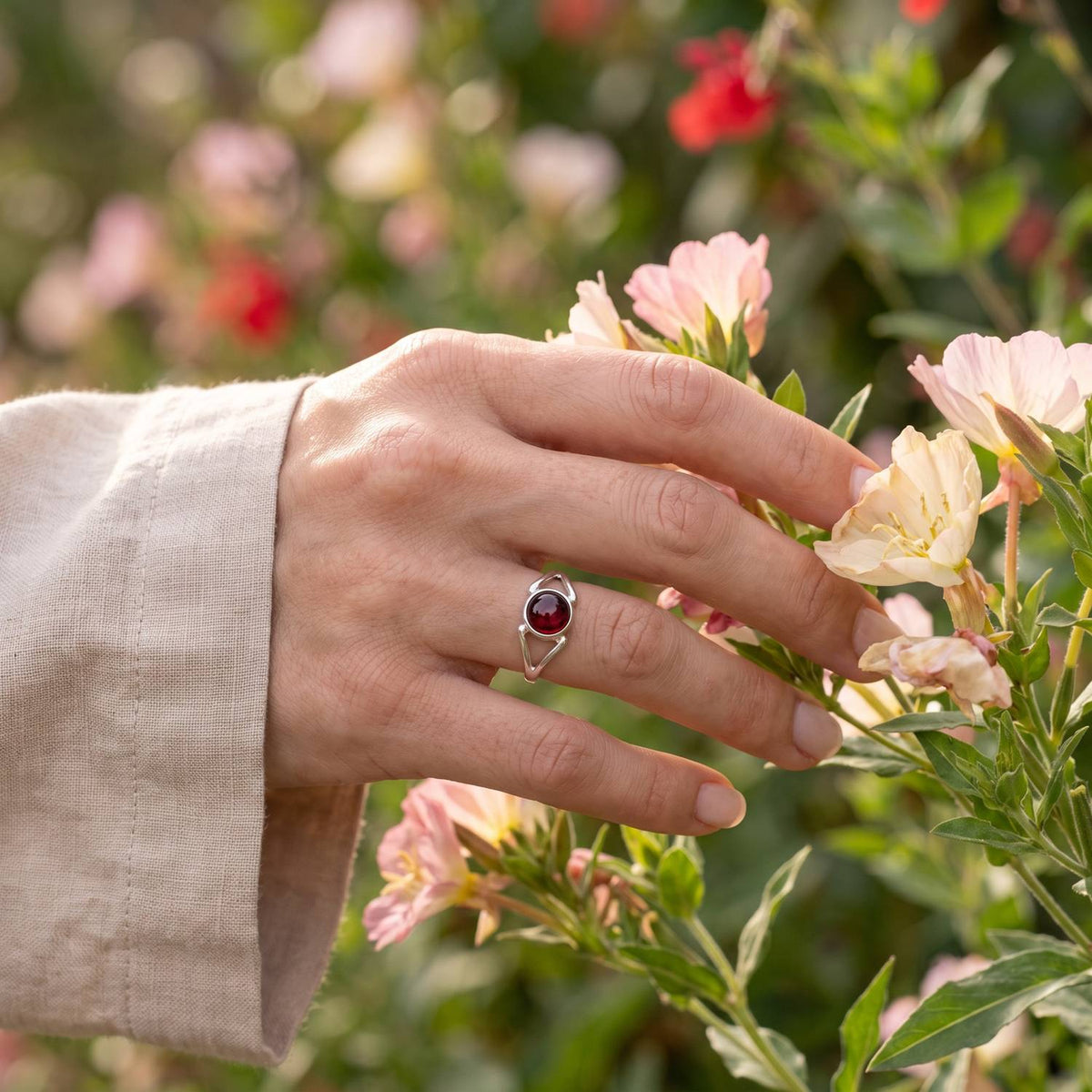 Silberring mit Granat an der Hand zwischen Blumen