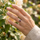[KI] Silberring mit Granat an der Hand zwischen Blumen