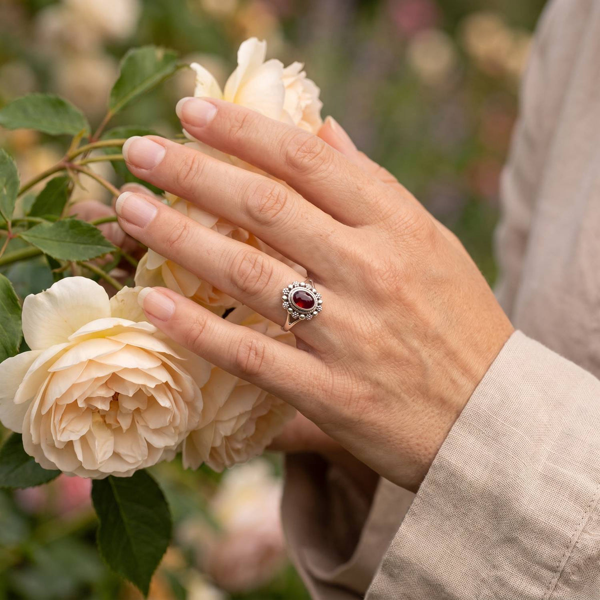 Silberring mit Granat an der Hand zwischen Blumen