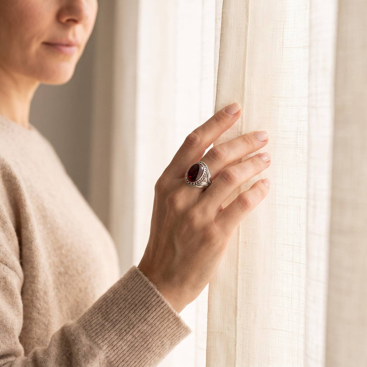 Frau trägt einen Granatring aus Silber am Fenster