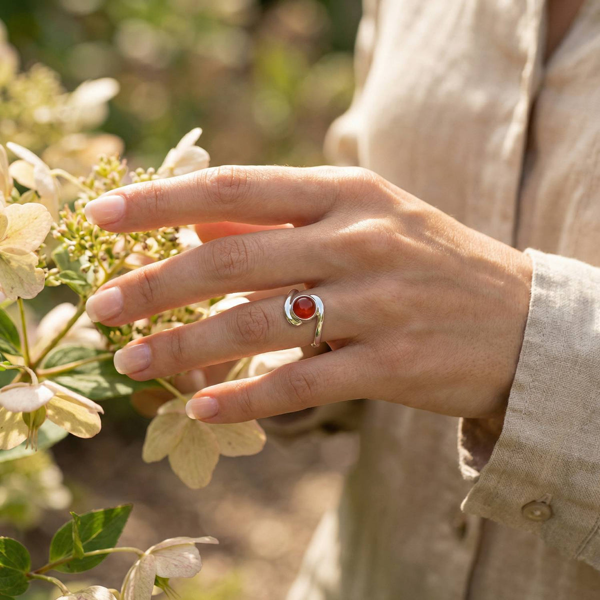 Silberring mit Karneol an der Hand zwischen Blumen