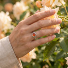 [KI] Silberring mit Karneol an der Hand zwischen Blumen