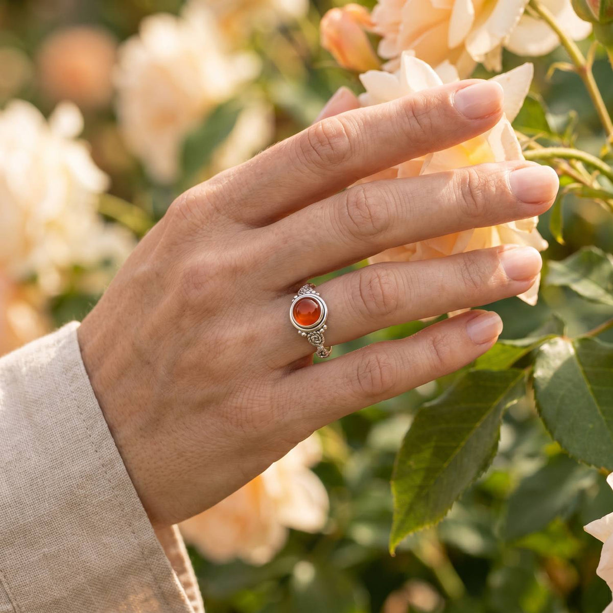 Silberring mit Karneol an der Hand zwischen Blumen