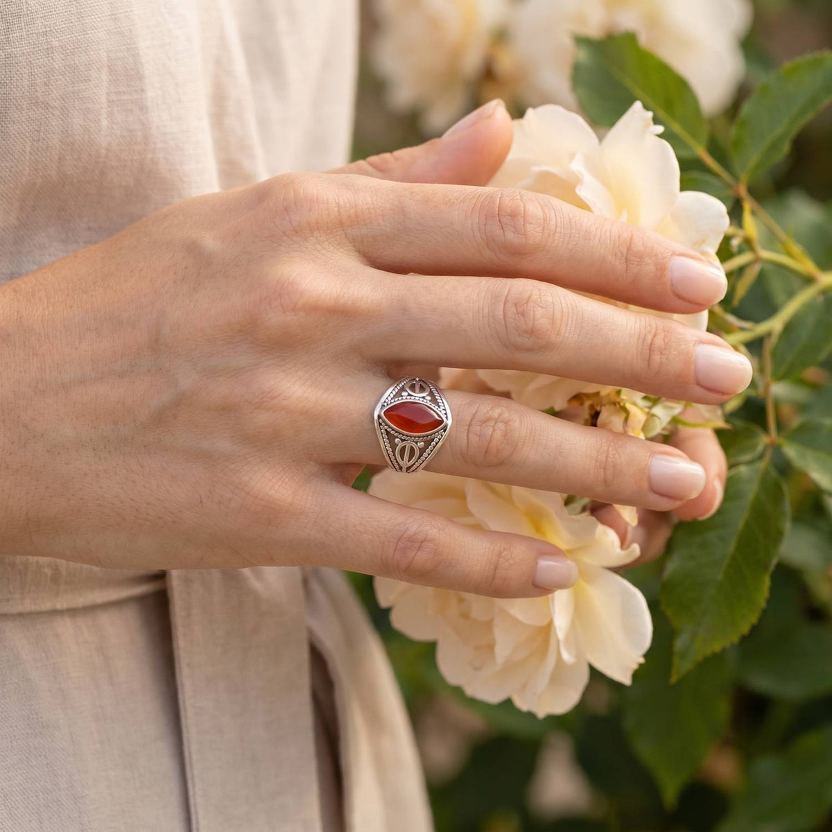 Silberring mit Karneol an der Hand zwischen Blumen