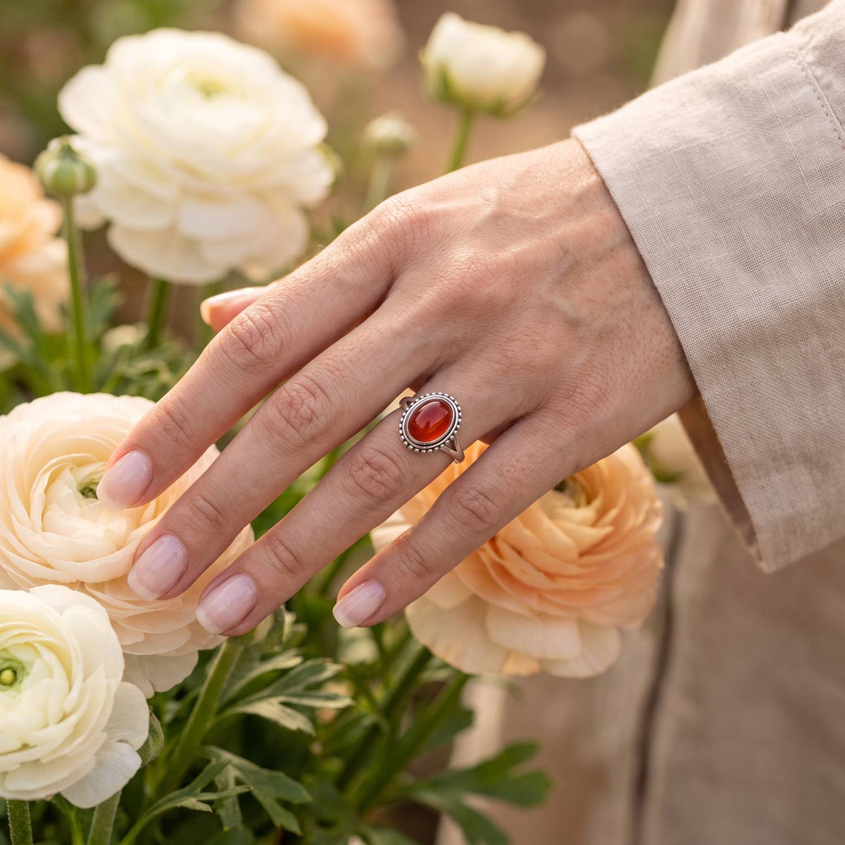 Silberring mit Karneol an der Hand zwischen Blumen