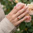 [KI] Silberring mit Karneol an der Hand zwischen Blumen