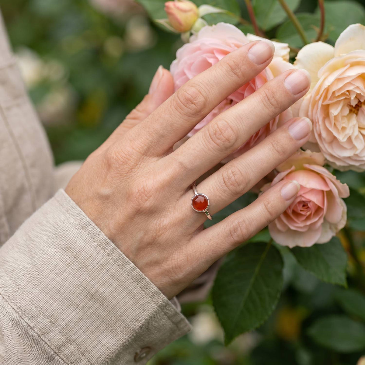 Silberring mit Karneol an der Hand zwischen Blumen