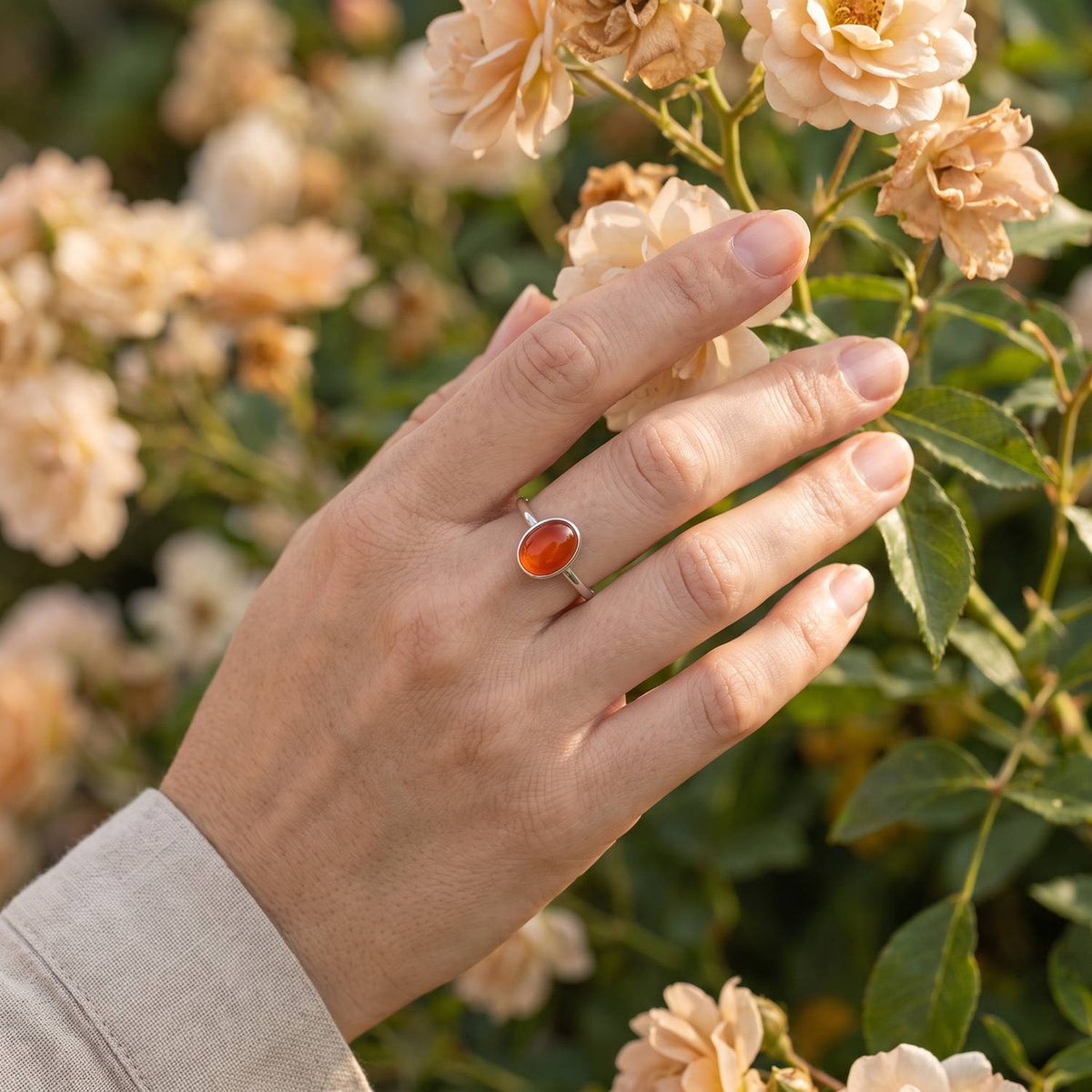 Silberring mit Karneol an der Hand zwischen Blumen