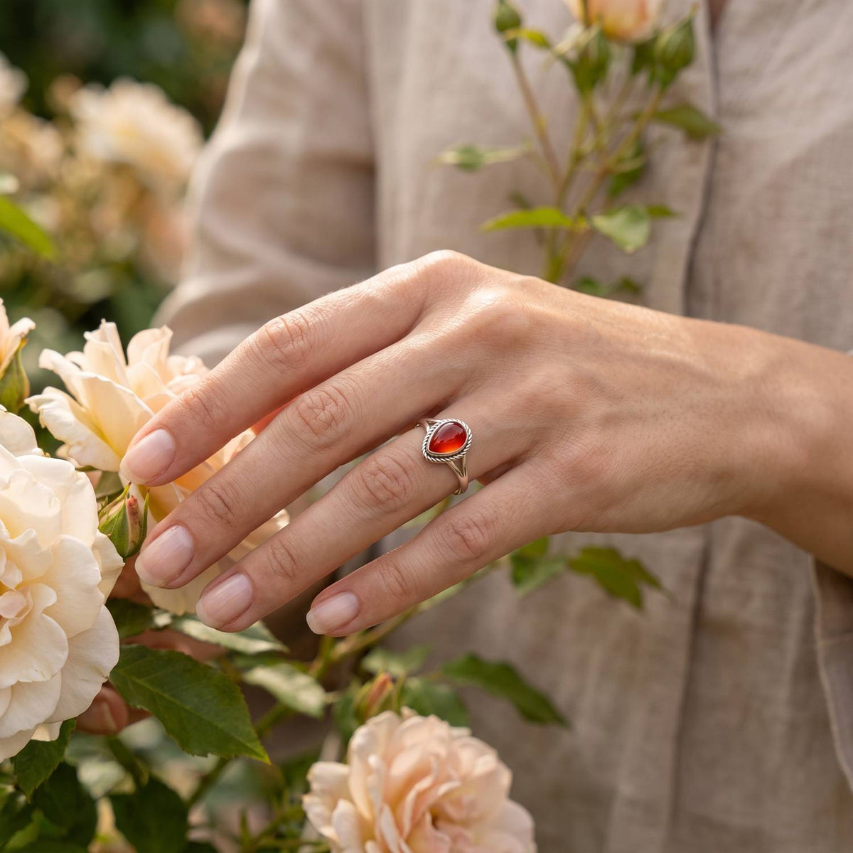 Silberring mit Karneol an der Hand zwischen Blumen