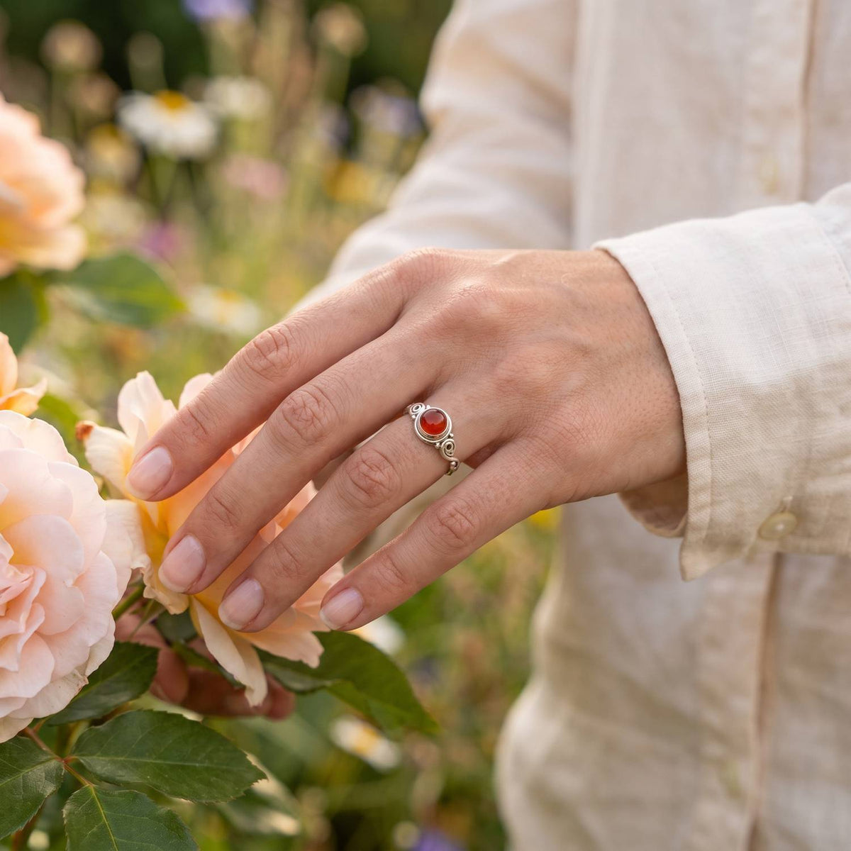 Silberring mit Karneol an der Hand zwischen Blumen