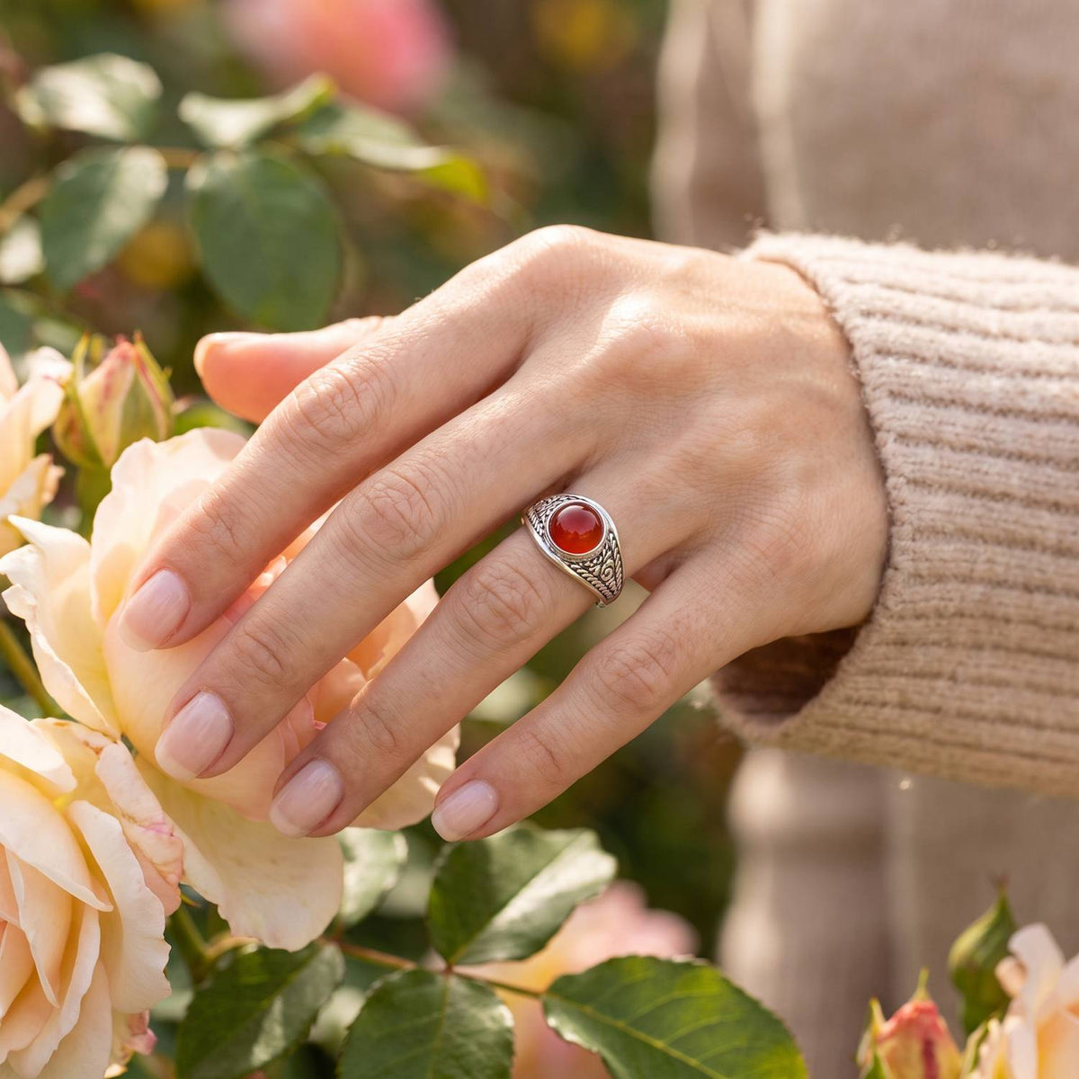 Silberring mit Karneol an der Hand zwischen Blumen
