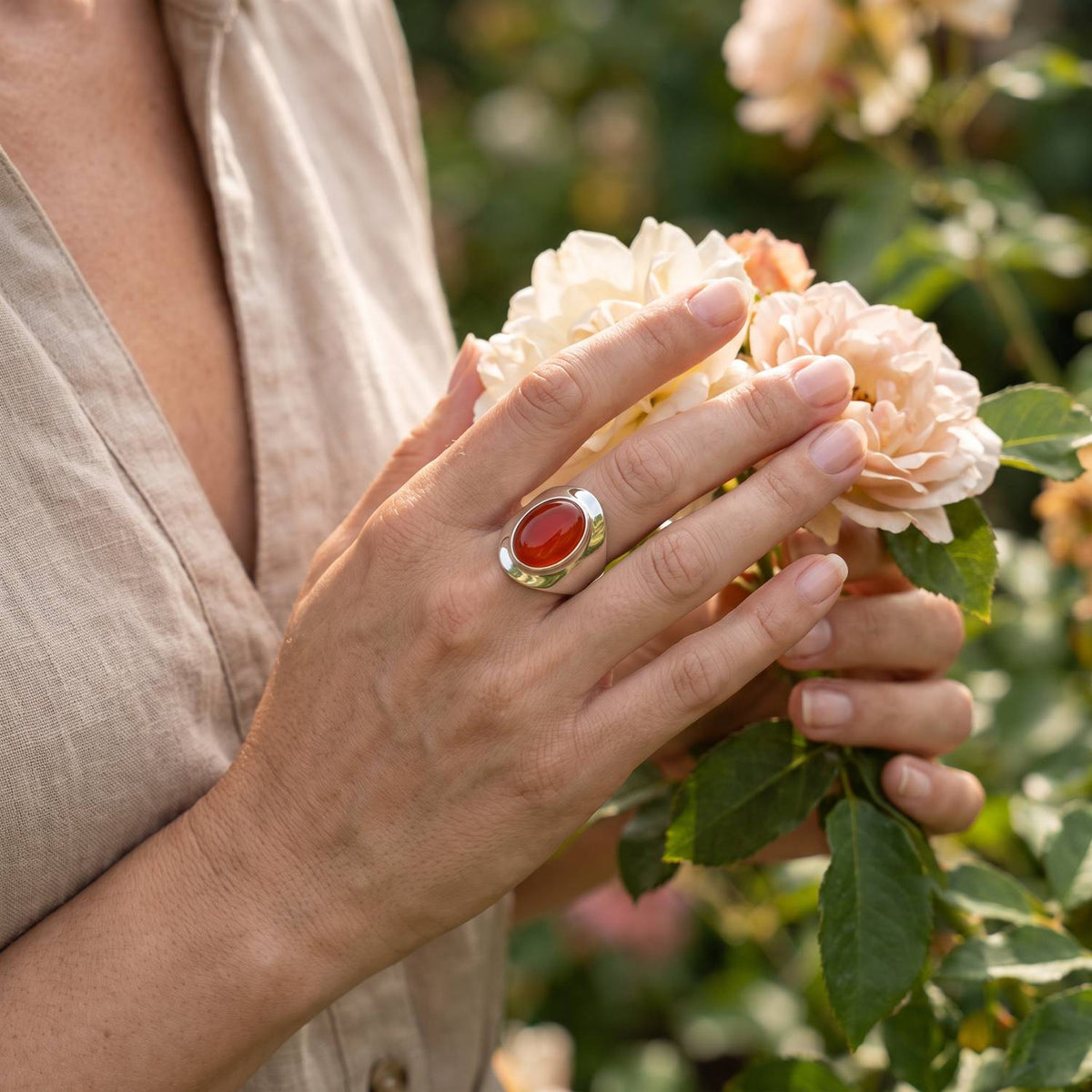 Silberring mit Karneol an der Hand zwischen Blumen