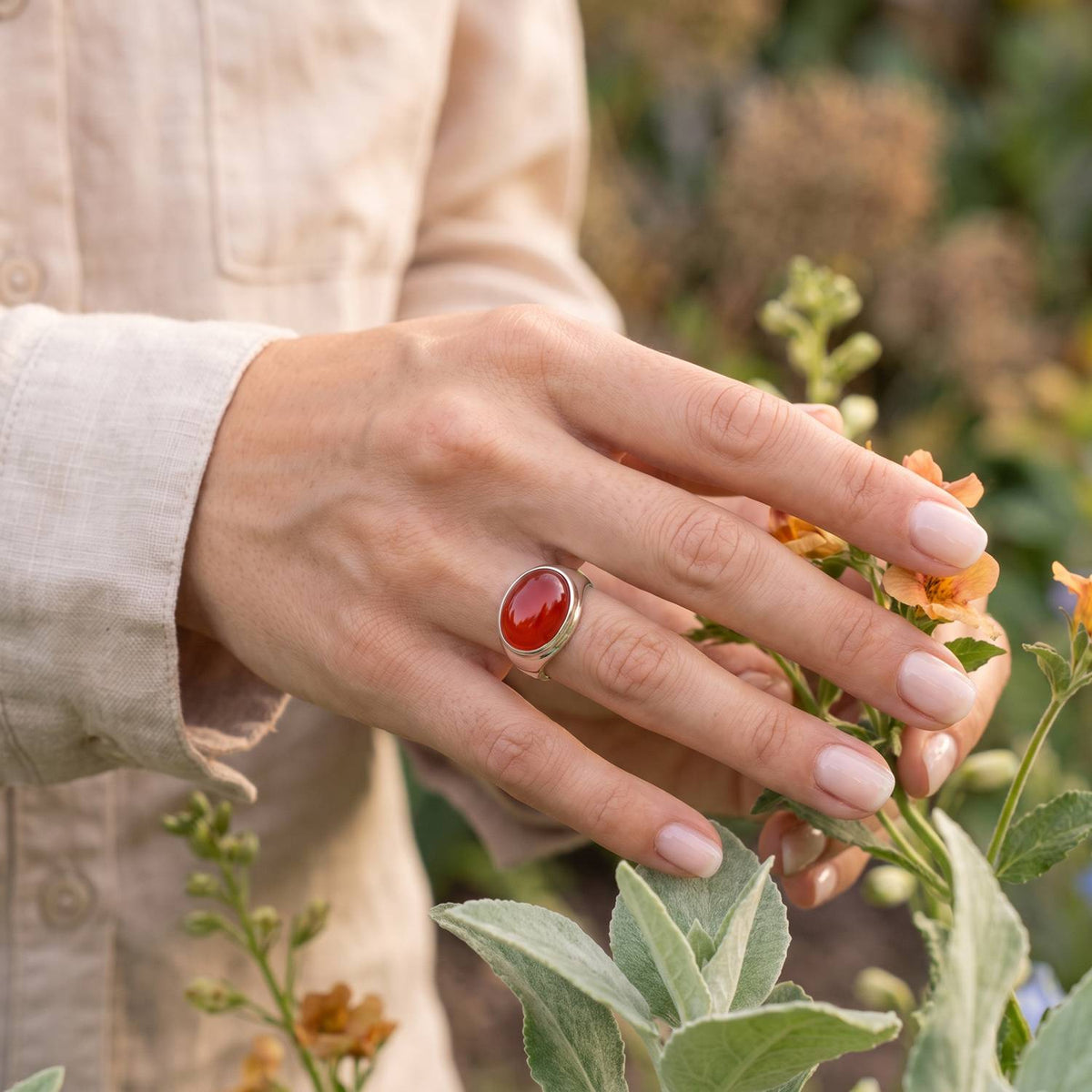 Silberring mit Karneol an der Hand zwischen Blumen