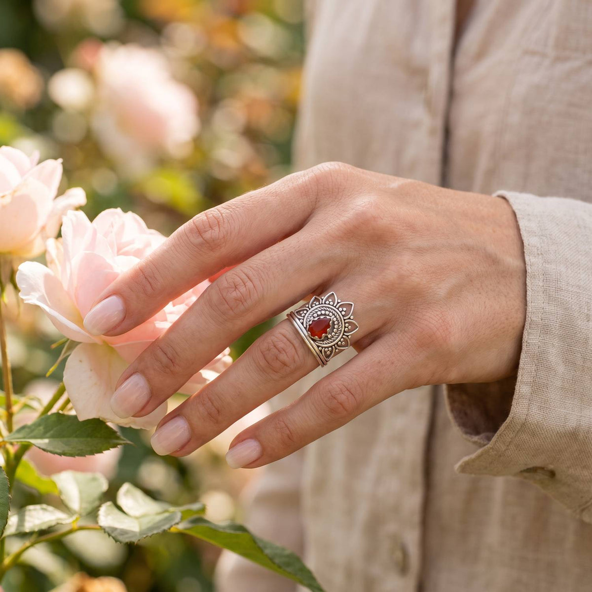 Silberring mit Karneol an der Hand zwischen Blumen