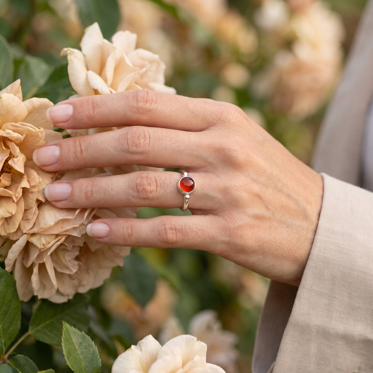 Silberring mit Karneol an der Hand zwischen Blumen