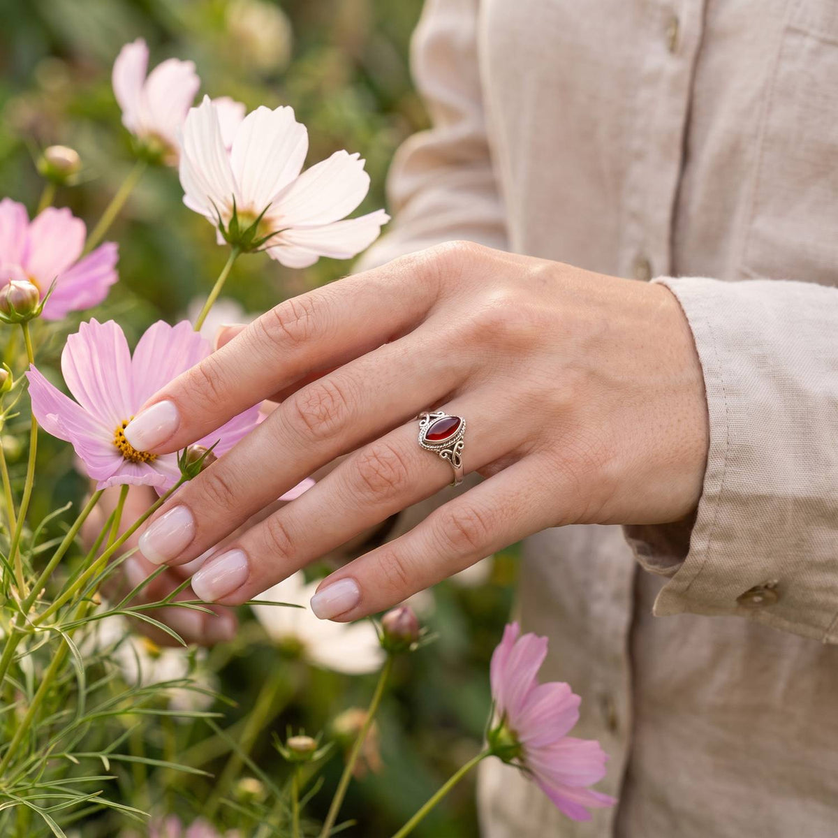 Silberring mit Karneol an der Hand zwischen Blumen