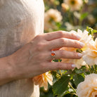 [KI] Silberring mit Karneol an der Hand zwischen Blumen