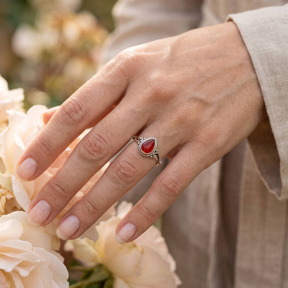 Silberring mit Karneol an der Hand zwischen Blumen