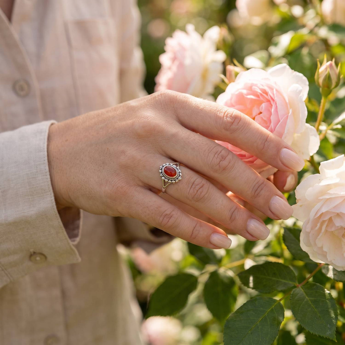 Silberring mit Karneol an der Hand zwischen Blumen