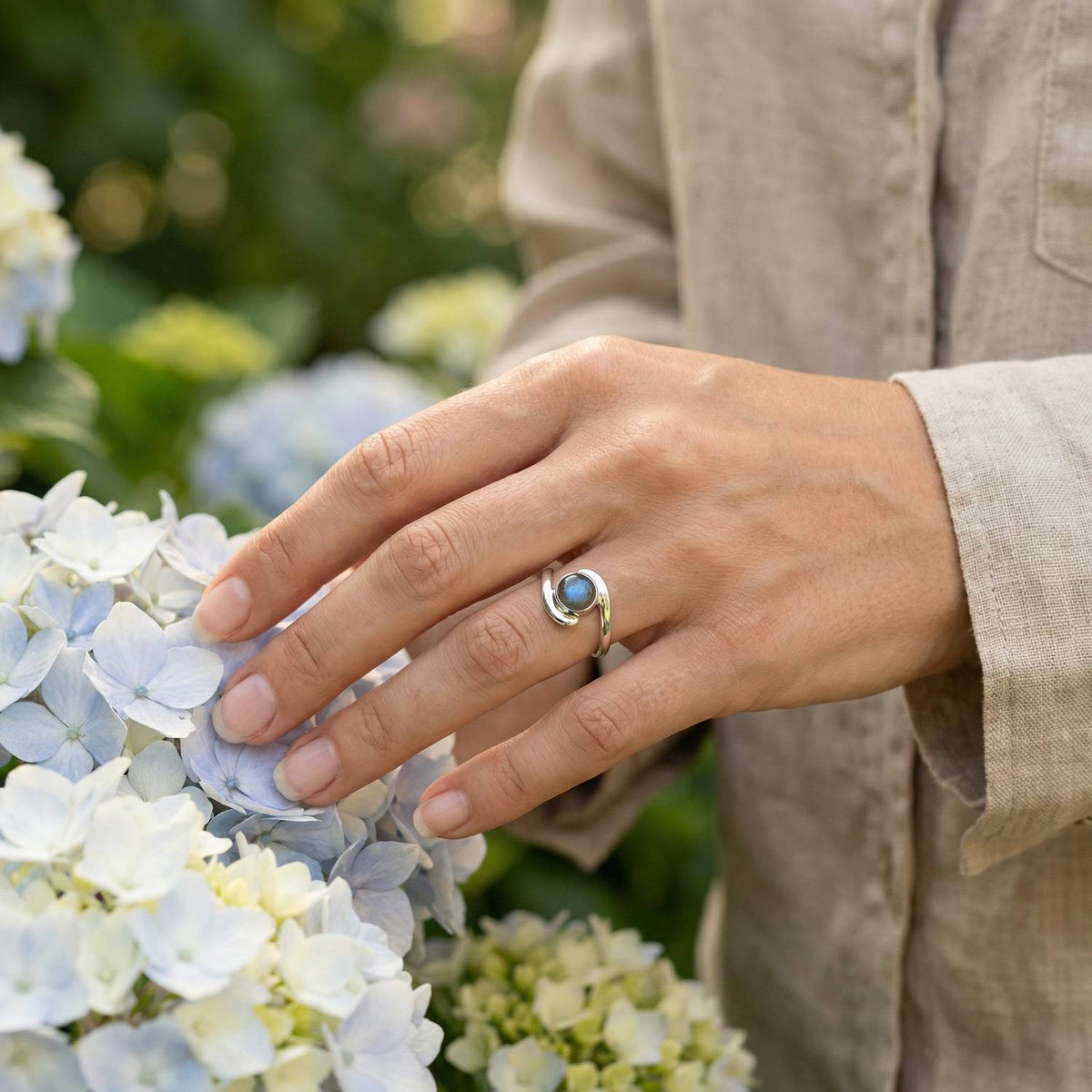 Silberring mit Labradorit an der Hand zwischen Blumen