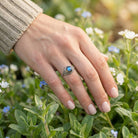 [KI] Silberring mit Labradorit an der Hand zwischen Blumen