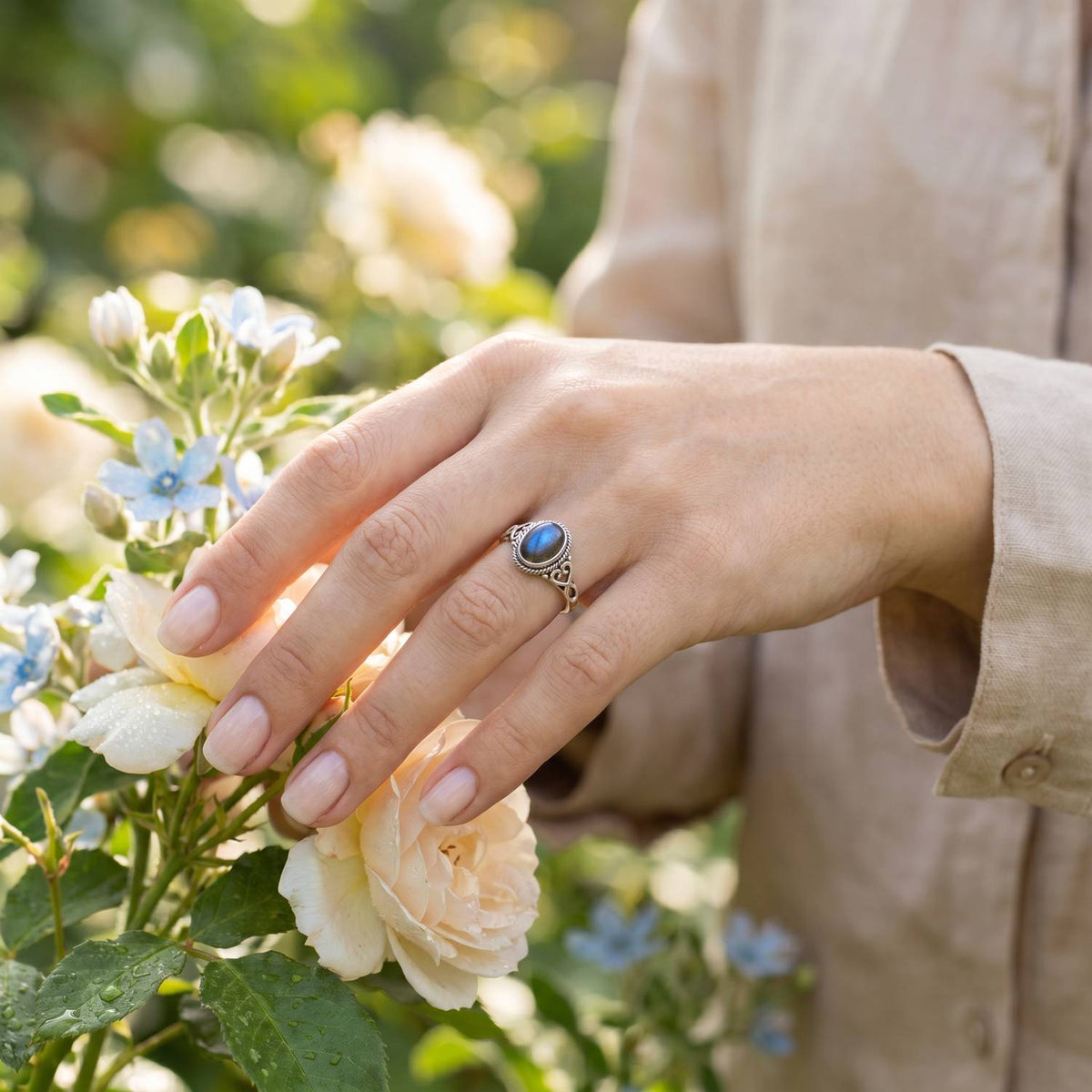 Silberring mit Labradorit an der Hand zwischen Blumen