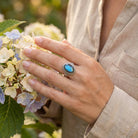 [KI] Silberring mit Labradorit an der Hand zwischen Blumen