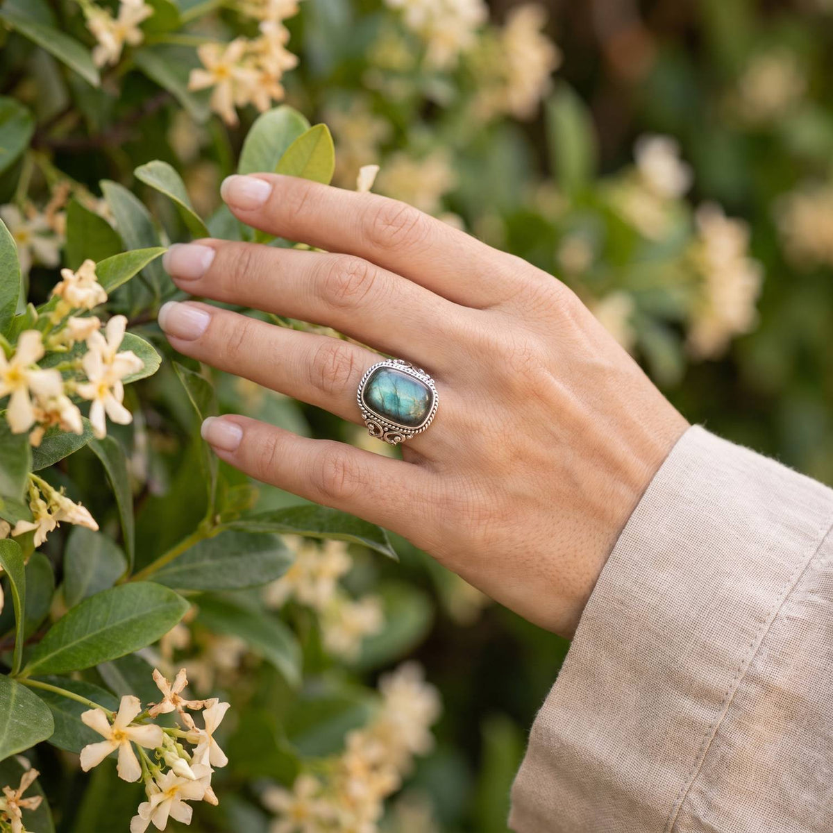 Silberring mit Labradorit an der Hand zwischen Blumen