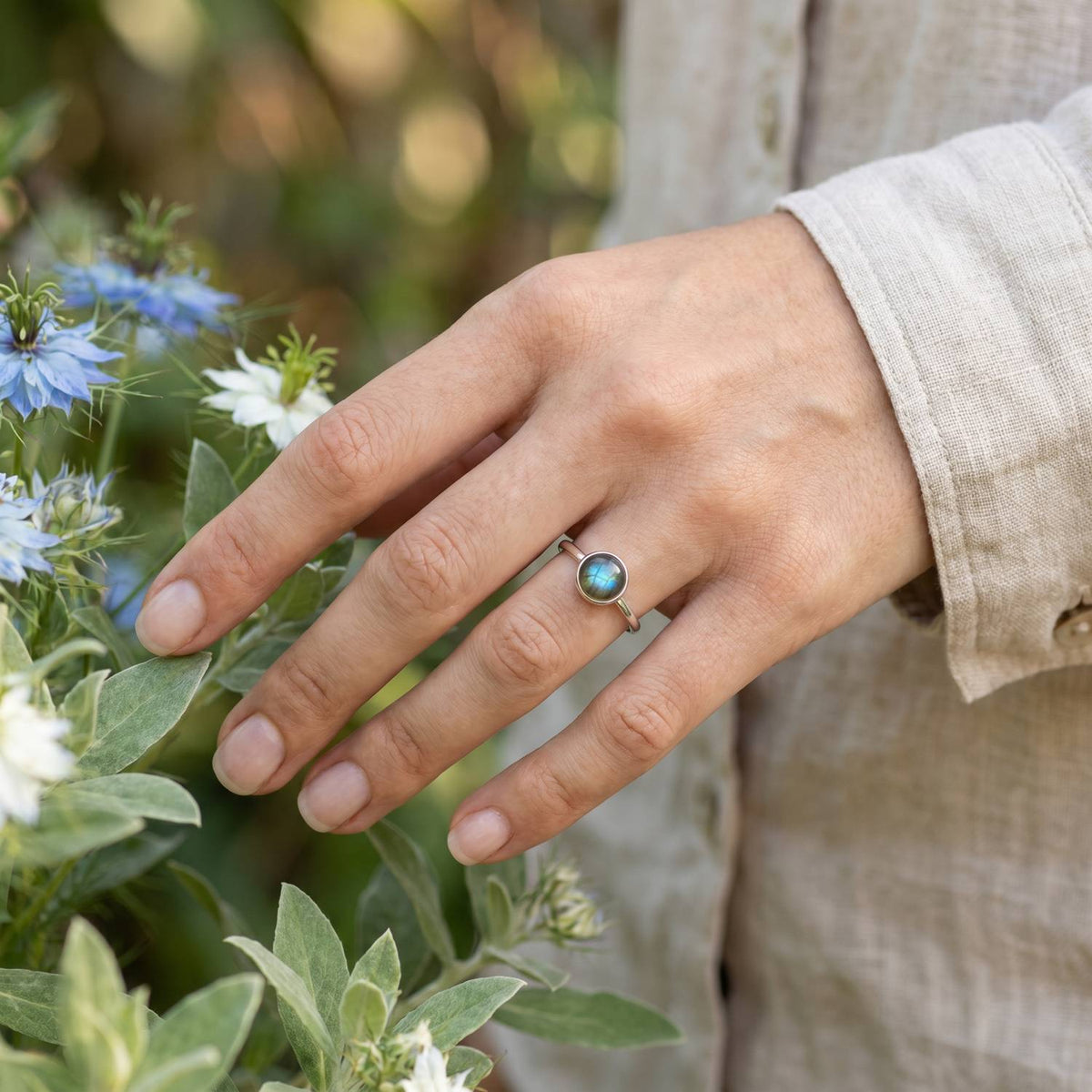 Silberring mit Labradorit an der Hand zwischen Blumen