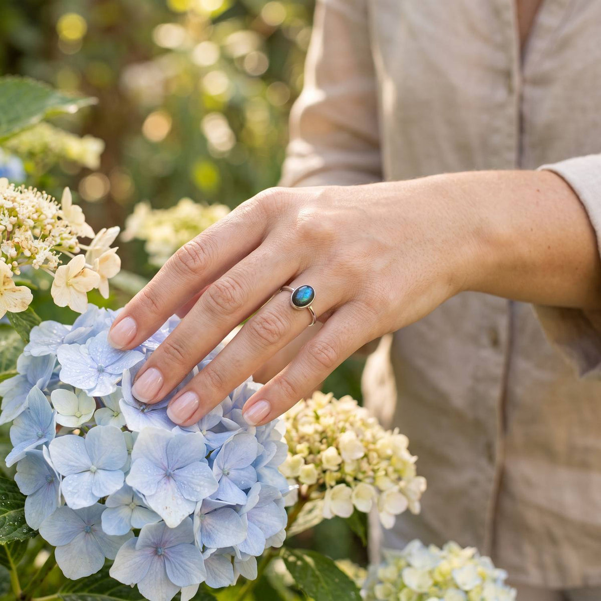 Silberring mit Labradorit an der Hand zwischen Blumen